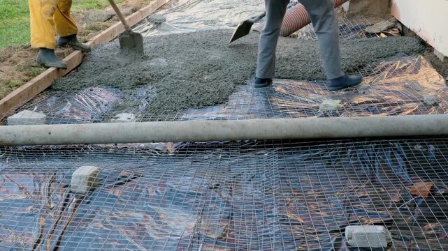 Two unrecognizable workers spreading the raw concrete near the house on a construction site
