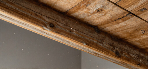 Close-up of weathered wooden beams and planks with visible knots and texture against a gray wall.