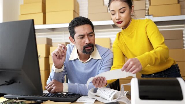 Business owner and employee labeling packages using printer and tablet in warehouse office