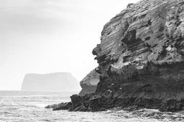 Black and white image of the volcanic rock formations on the cost of Bartolome Island in the Galapagos archipelago - Daphne Minor in the background
