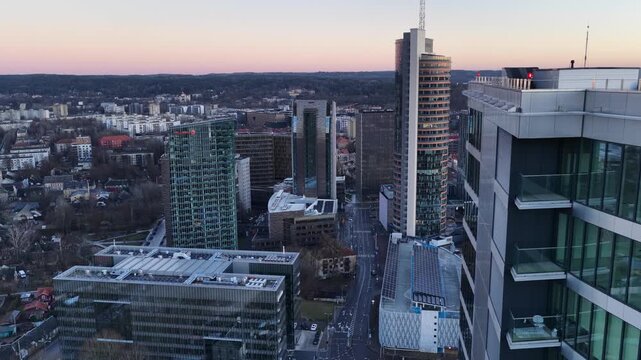 Panoramic aerial shot of Vilnius cityscape during sunset, showcasing modern skyscrapers, commercial buildings, and the iconic Vilnius TV Tower in the background.
