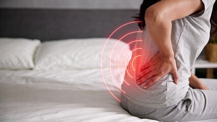 Woman suffering from lower back pain sitting on bed at home