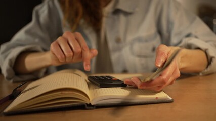 Cautious woman at a wooden table counting dollar bills and recording monthly expenses and utility payments in a notebook while managing household budget at home, focused on finances - Powered by Adobe