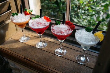 Four different colored drinks in martini glasses with straws
