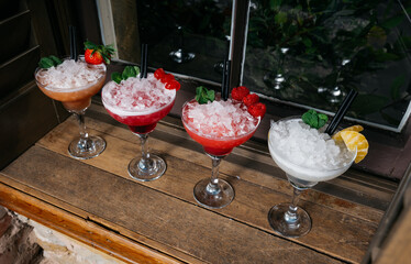 Four different colored drinks in martini glasses with ice and fruit garnish
