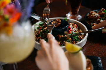 A group of people are eating food at a table with a bowl of food in the middle