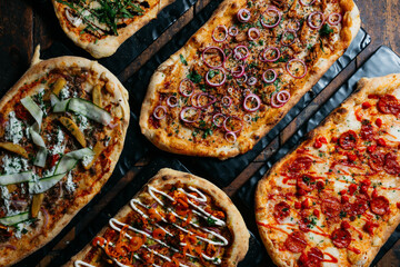 A row of pizzas with various toppings, including pepperoni, onions, and cheese