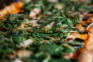 A pizza with green leaves on top and a sauce drizzle