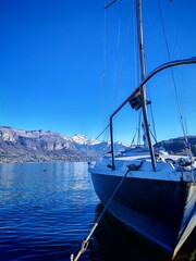Fototapeta premium Sailing boat is at the harbour of Annecy lake. Snow-capped mountains Mont Baret in the background