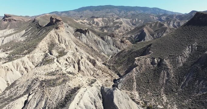 Aerial view of eroded desert badlands with rugged ridges and dry valleys stretching across the Tabernas Desert landscape of Andalusia Spain under clear blue sky