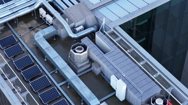 Detailed aerial view of a commercial building rooftop featuring solar panels, HVAC units, air ducts, and ventilation structures, showcasing sustainable and functional architecture elements.
