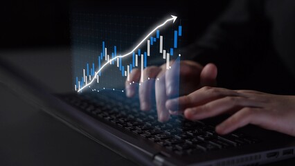 A person types on a laptop keyboard while a digital financial chart overlays the scene, illustrating market trends and upward growth in a modern setting. Copula