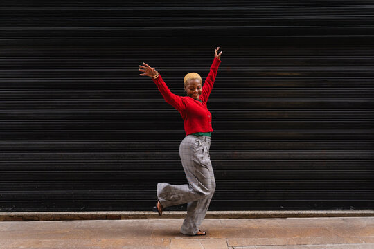 Happy young black woman dancing in front of a contrasting black background feeling joyful
