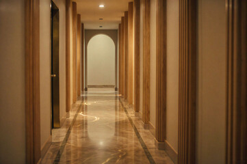 A long hallway with polished marble floor, wooden pillars, and warm lighting leading to an arched doorway.