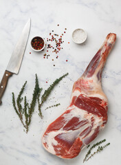 A raw whole shoulder of lamb on a marble table, spices - pepper, salt, garlic and fresh thyme. Selective focus