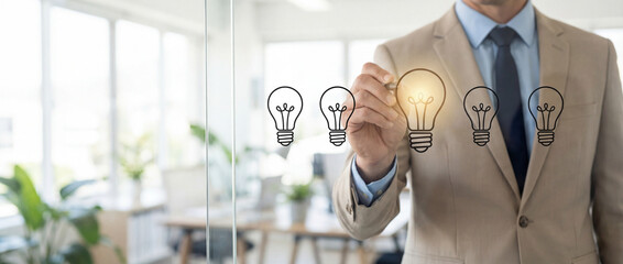 Businessman in a tan suit interacting with a glowing light bulb graphic on a transparent virtual interface in a bright modern office, symbolizing innovation and creative business solutions.