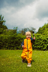 Joyful child in bright orange outfit playing in a green garden under a cloudy sky