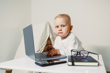 Little expert works on laptop while surrounded by books and a smartphone in a cozy home office setting