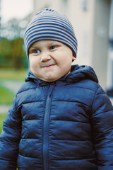 Happy child wearing a blue puffer jacket and striped beanie smiles joyfully in a park during a sunny afternoon