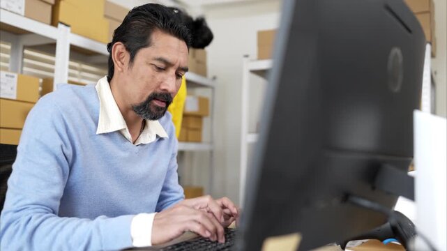 Business owner and employee labeling packages using printer and tablet in warehouse office