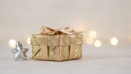 Elegant gold glitter gift box with satin ribbon and star ornament, soft bokeh lights