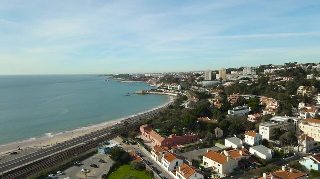 Aerial orbit over Portugal Caxias coastal neighborhood with red-roof houses beside the Tagus River on a sunny day.