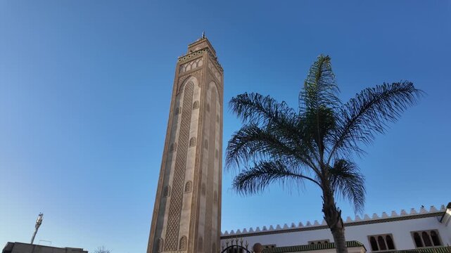 Mosque minaret towering against a clear blue sky, displaying traditional moroccan architecture alongside a vibrant palm tree in marrakech, morocco