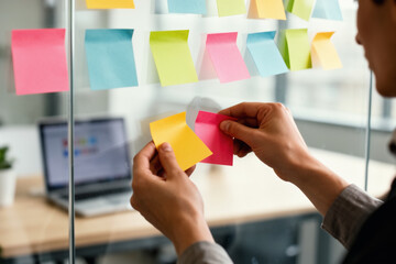 Hands adding sticky note to glass team workflow board.