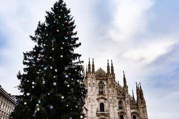 Duomo di Milano cathedral with Gothic spires and detailed marble fa&ccedil;ade under a bright blue sky. With a Christmas tree