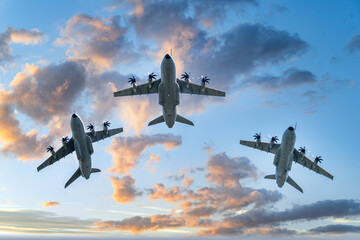 Three airbus a400m atlas transport aircraft flying in a tight triangular formation at sunset with visible propellers, striking wing contours and dramatic cloudscape