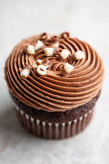 Close up of a chocolate cupcake topped with rich chocolate cream cheese frosting and chocolate curls on a soft light stone background. Dessert menu.