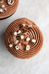 Chocolate cupcake with swirled cream cheese frosting with chocolate curls top view, a minimal high-key dessert on a white stone background.