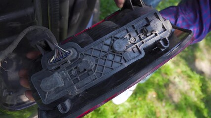 Human hands remove the rear light from the vehicle, A person holds a car rear light in his hands, Repair or installation: rear light in the hands of a mechanic