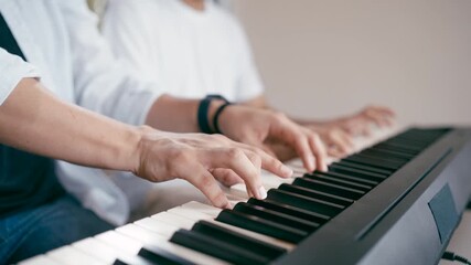 Close up of four hands playing a digital piano. A music instructor teaches a student how to play a melody on an electronic keyboard - Powered by Adobe