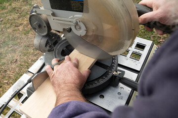 Hands of a man using a chop or miter saw to cut wood.
