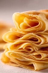 Delicate golden crepes, folded and stacked, preparing a sweet or savory meal. Freshly made and ready to eat
