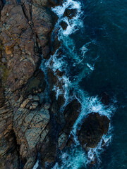 Waves crashing against rugged rocks under the afternoon sun near a tranquil coastal village surrounded by nature's beauty and vibrant energy