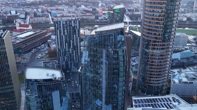 Panoramic aerial shot of Vilnius cityscape during sunset, showcasing modern skyscrapers, commercial buildings, and the iconic Vilnius TV Tower in the background.