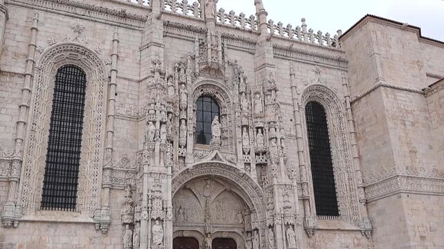 Upward pan revealing the richly carved stone entrance of Jeronimos Monastery with intricate statues and historic facade, no people visible