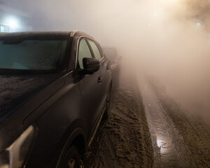 Steam and hot water from a burst central heating pipe fill a city street with fog, cars parked along a flooded winter roadway.