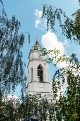 Church of the Annunciation of the Blessed Virgin Mary in Tula city, Russia. A tent-shaped bell tower between the branches of trees against blue sky