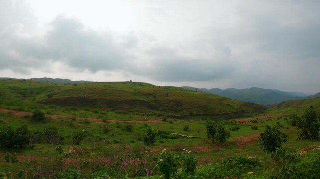4K view of green Sahyadri hills as seen from moving vehicle at Rayta village, Udaipur, India. Green trees and grass on hills and clouds in sky during monsoon season. Road trip, travel and vacation con
