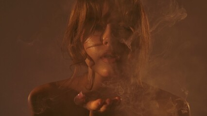 A close up of a woman in dim lighting blowing smoke, creating a mystic and atmospheric ambiance. © kinomaster