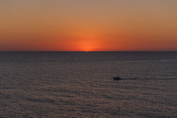 Naklejka premium A boat cruising on calm sea at dawn or dusk.