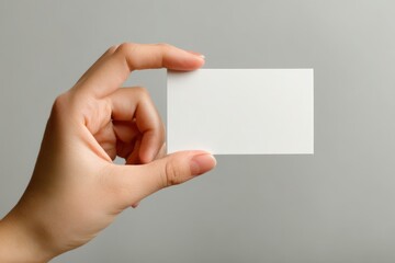 Fototapeta premium Minimalist shot of a hand presenting a plain white card on a neutral background