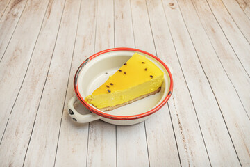 Triangular slice of baked New York cheesecake with a golden crust and creamy center, served with raspberry sauce and fresh mint leaves on a black plate