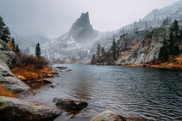 Misty autumn mountain lake with fog, a snow-capped peak and rugged shoreline