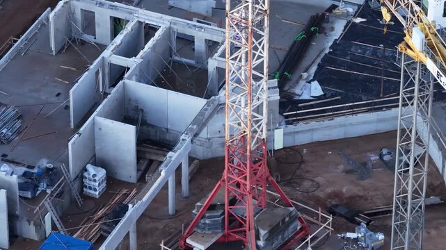 Close-up aerial view of a reinforced concrete building under construction. Exposed interior walls, scaffolding, and tower crane base are visible, showing early development stages.