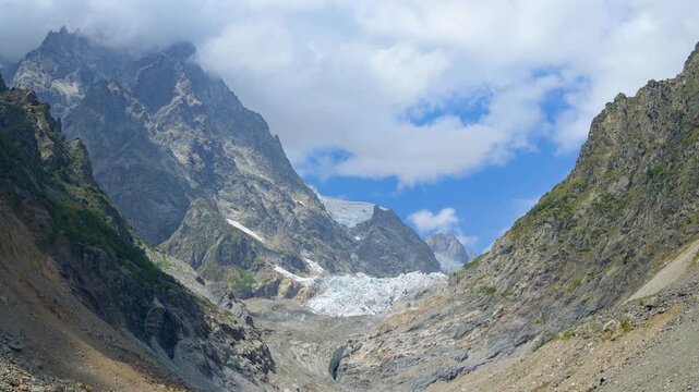 Timelapse of a glacier valley with high mountains and moraines, as fast-moving clouds wrap around the peaks and flow through the landscape. Dramatic alpine atmosphere and natural motion.