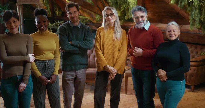 Smiling multiethnic group therapy participants and therapist standing together and looking at camera, expressing satisfaction, unity, and success in modern interior with greenery.
